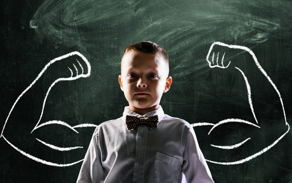 school boy is standing with strong hands on blackboard behind him